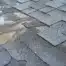 Close-up of damaged asphalt shingles on a roof showing wear, missing sections, and exposed underlayment.