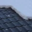 Top view of a roof, with black shingles, during winter with snow covering half of it.
