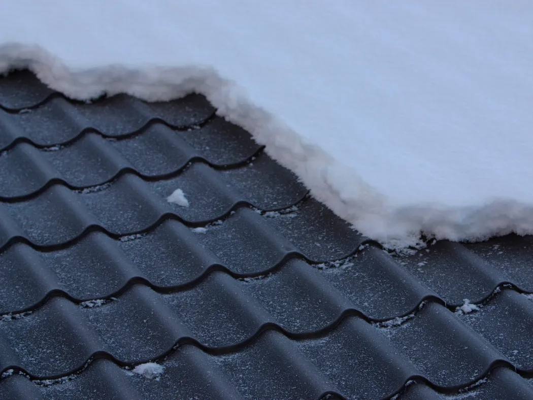 Top view of a roof, with black shingles, during winter with snow covering half of it.